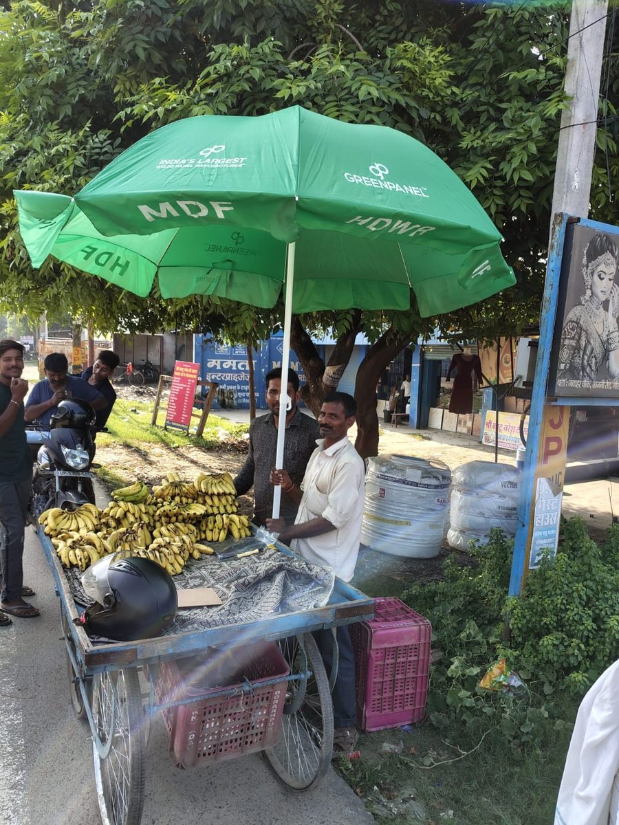 Greenpanel branded umbrella over a street fruit vendor's cart